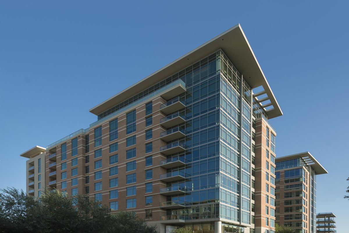 Hanover Company Modern multi-story apartment building with glass windows, surrounded by trees, under a clear blue sky.
