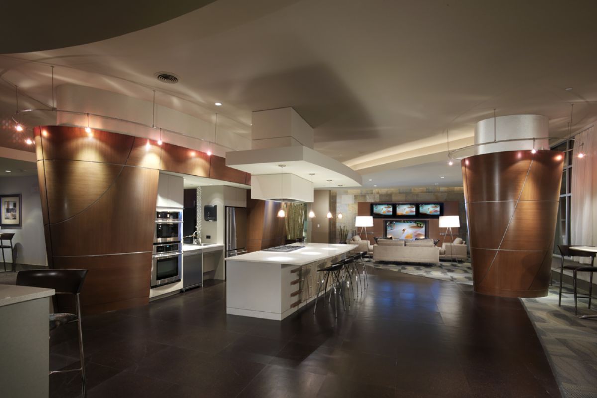 Modern lounge with curved wooden columns, a central island, bar stools, and TVs in the background.