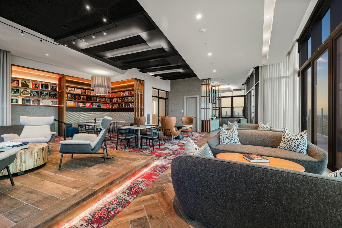 Modern lounge with plush seating, decorative rug, bookshelves, and large windows with city views.