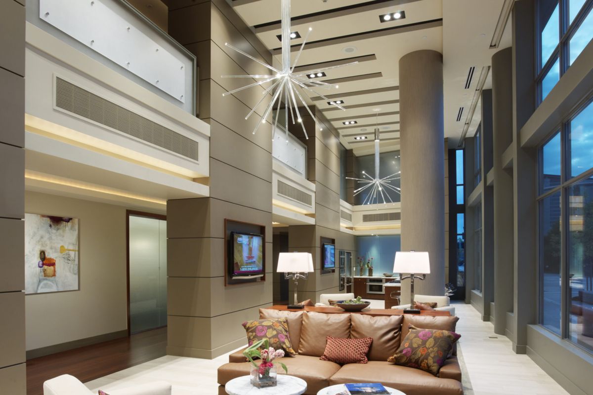 Modern hotel lobby with tall ceilings, stylish furniture, large windows, and contemporary lighting fixtures.