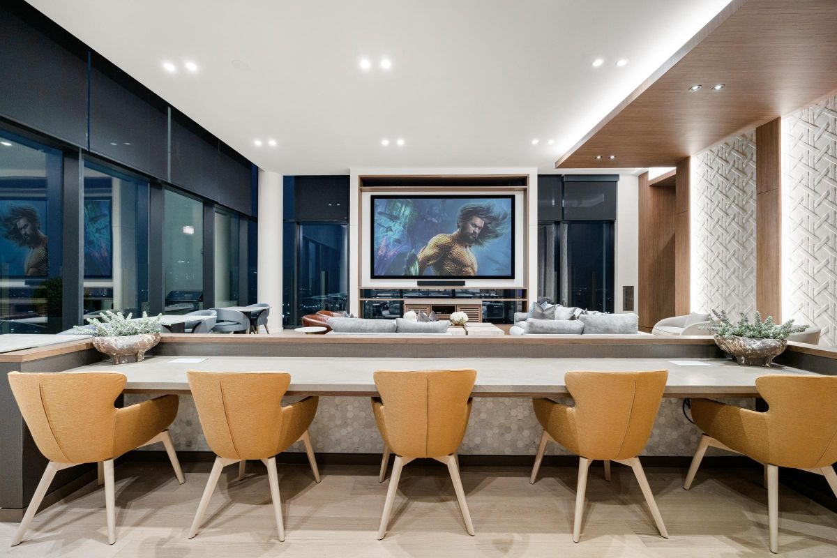 Modern lounge with yellow chairs, long table, and TV on the wall. Large windows show a night cityscape.