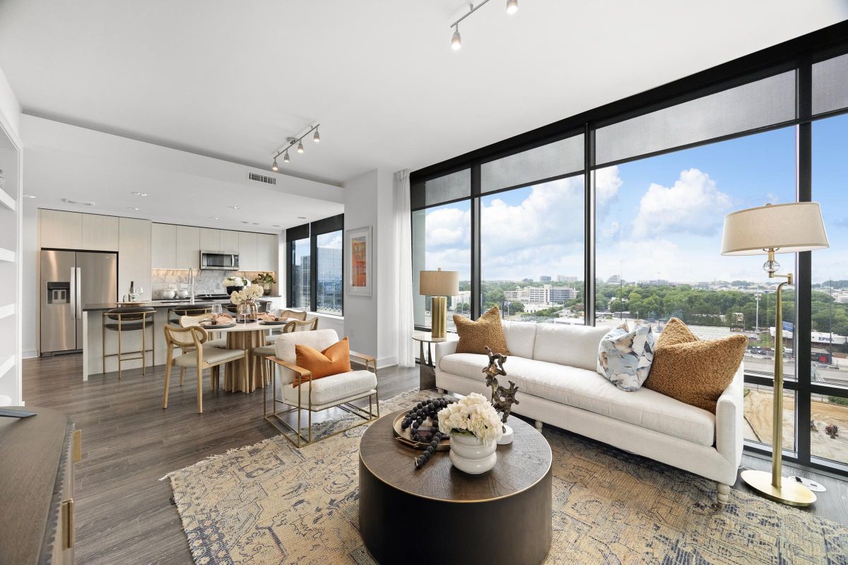 Modern living room with large windows, stylish furniture, a round coffee table, and cityscape view in the background.