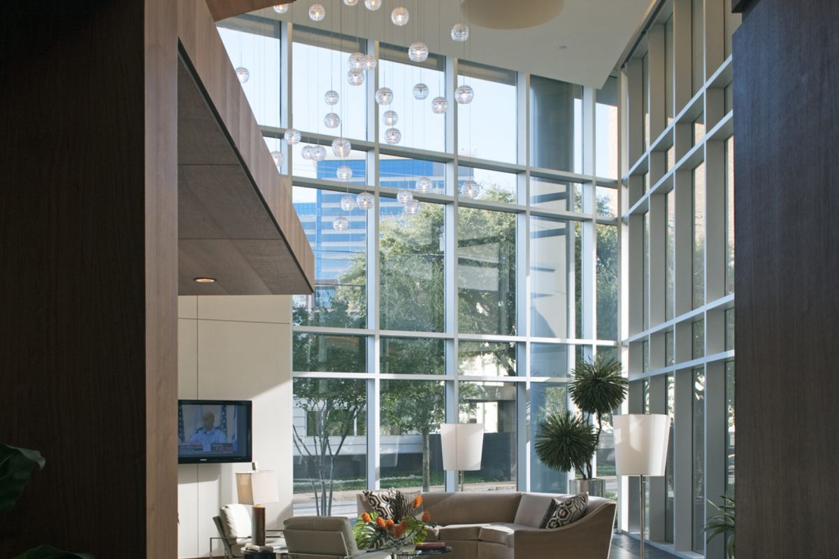 Modern lobby with floor-to-ceiling windows, stylish furniture, plants, and hanging glass sphere lights.