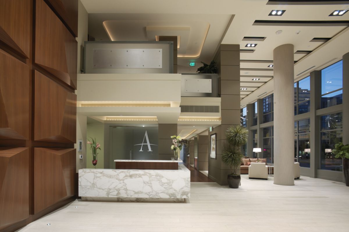 Modern hotel lobby with marble reception desk, wood accents, large windows, and indoor plants.