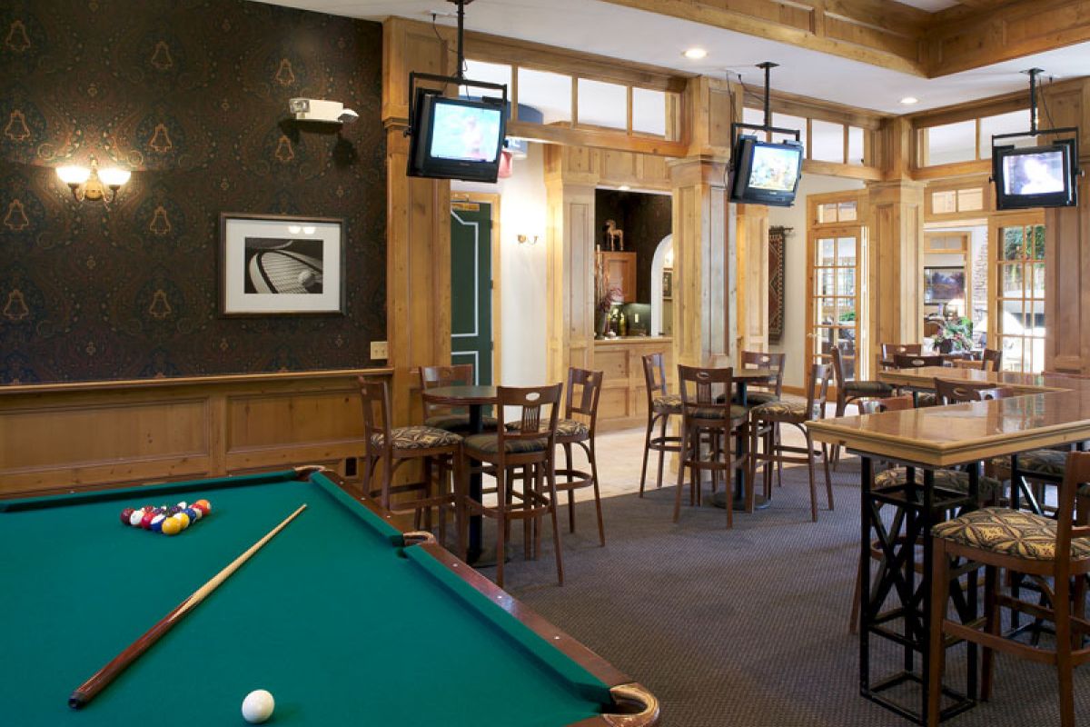 A pool table in a cozy bar with tables, chairs, wall art, and multiple TVs mounted on the walls.