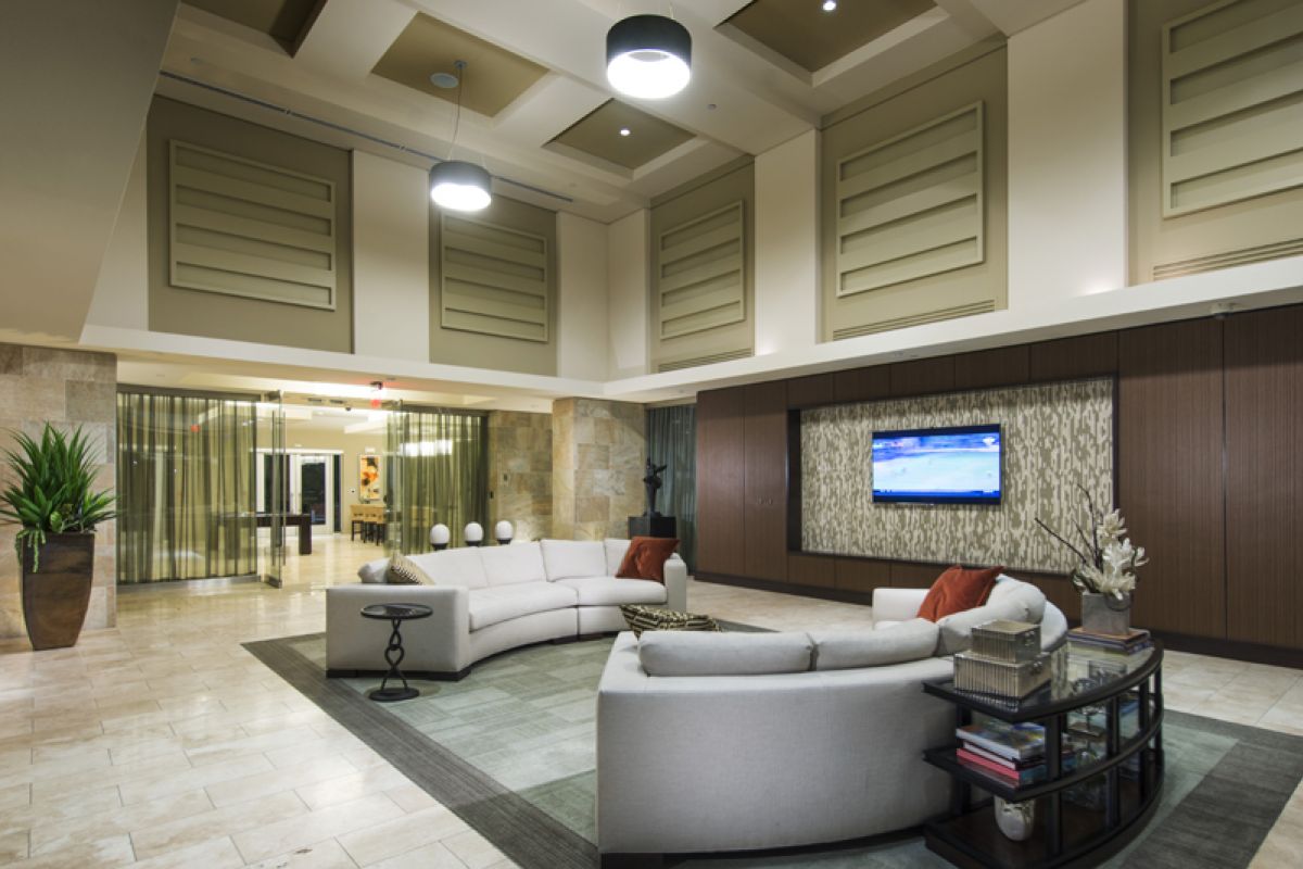 Modern lobby with curved sofas, a wall-mounted TV, plants, and large windows in a spacious, well-lit area.
