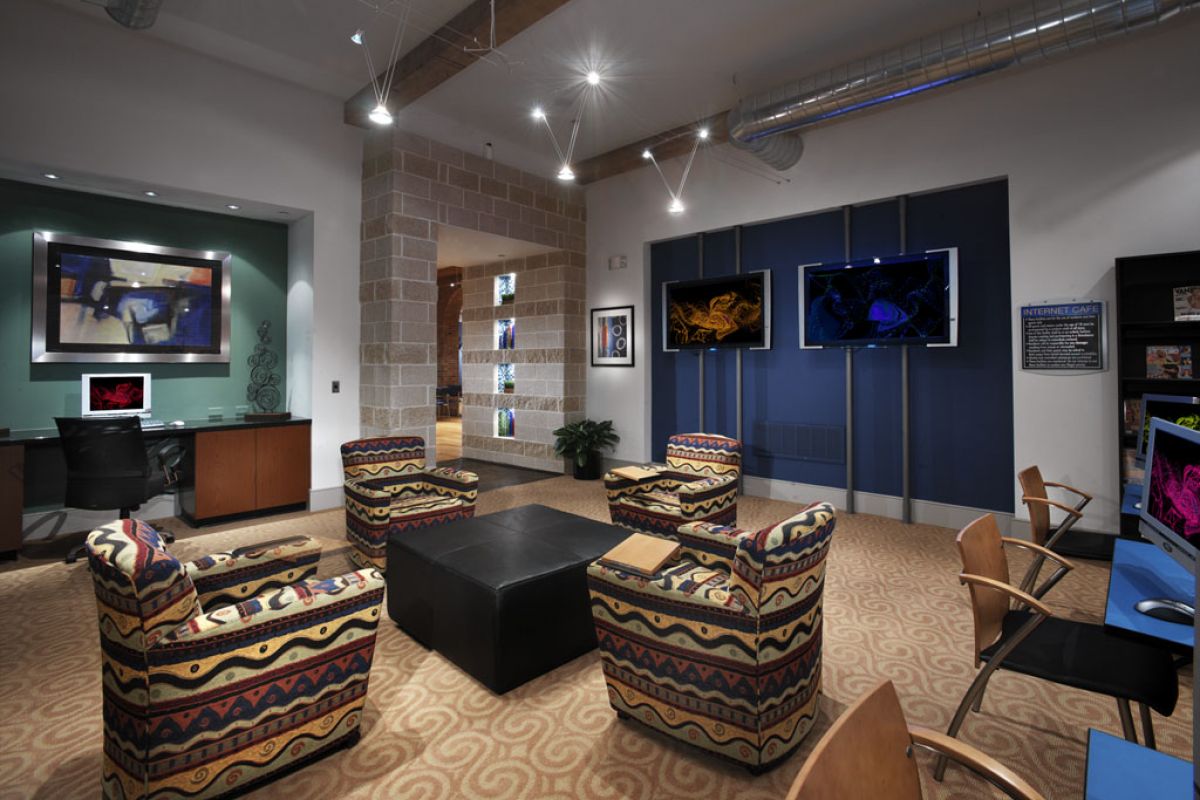 Modern office lounge with patterned chairs, a black ottoman, wall art, and flat-screen TVs mounted on a blue wall.