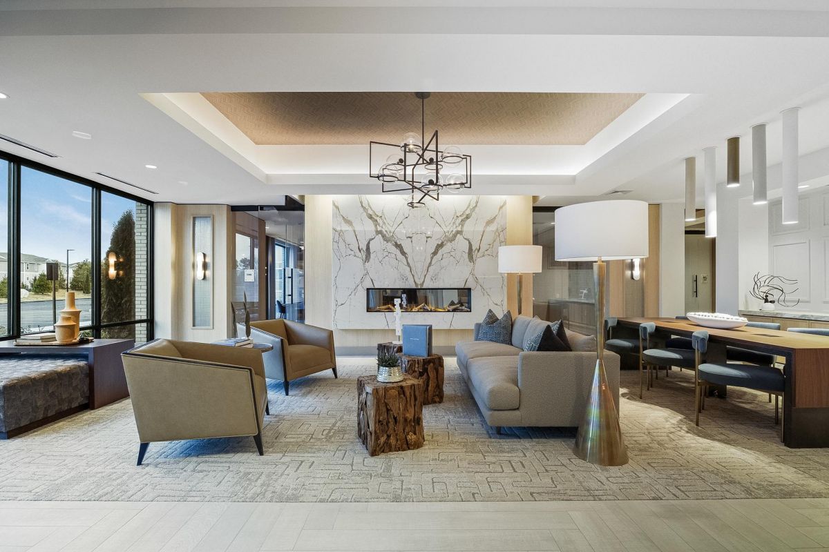 Modern living room with elegant furniture, a marble fireplace, large windows, and a geometric chandelier.