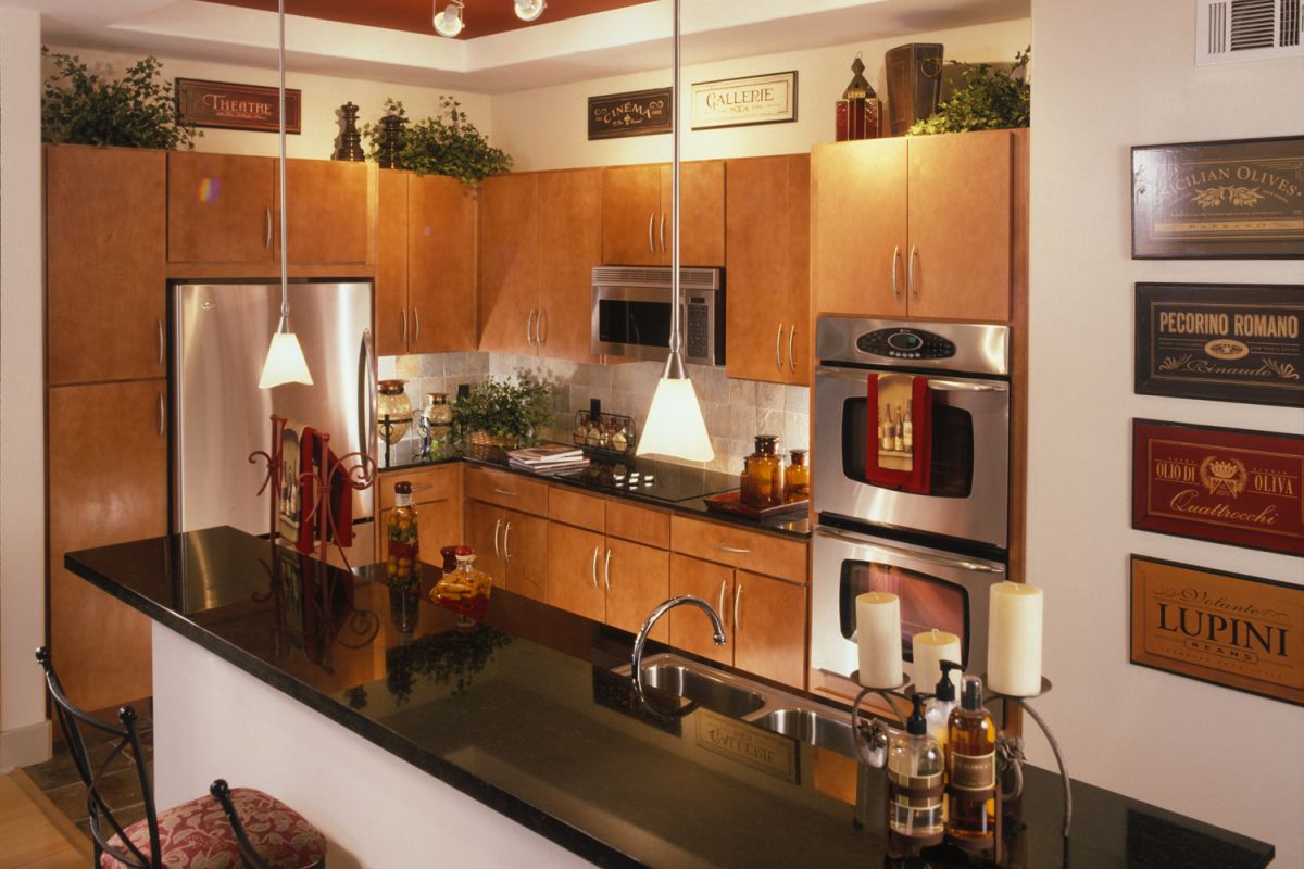Modern kitchen with wood cabinets, black countertops, stainless steel appliances, and decorative wall signs.