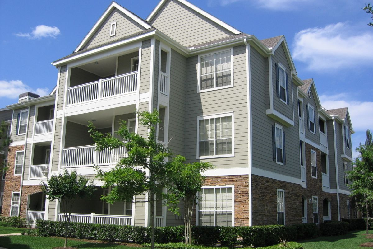 Modern three-story apartment building with balconies and large windows near the Broadwater Galveston, landscaped with grass and trees.