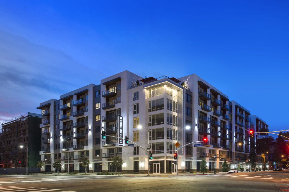 Modern apartment building at a city intersection during twilight, with streetlights and clear blue sky.