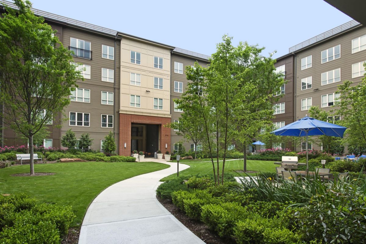 Landscaped courtyard of a modern apartment complex with green lawn, trees, and outdoor seating area.