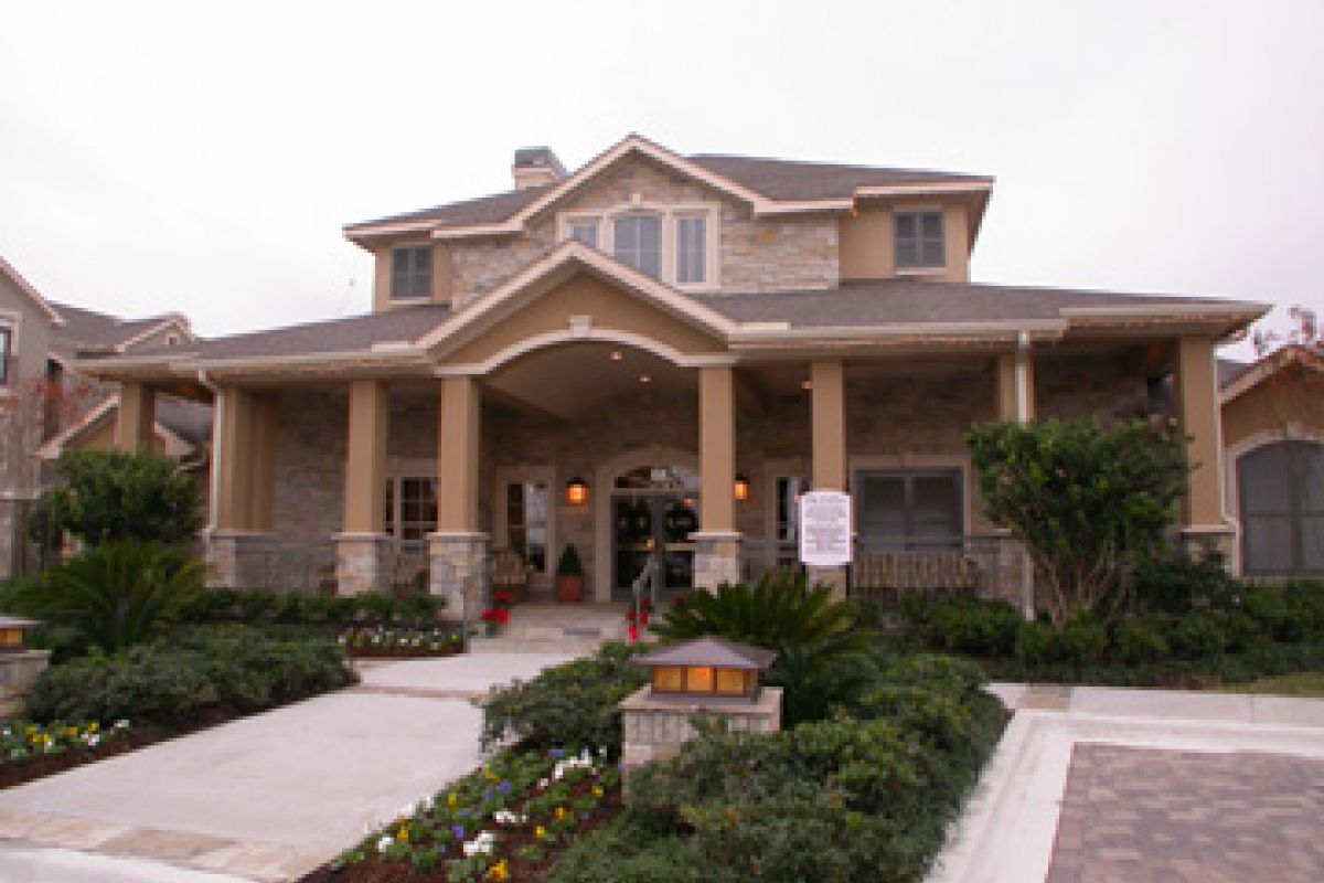 Two-story suburban house with stone facade, large front porch, columns, and landscaped garden.