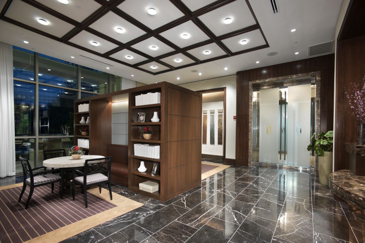 Modern office lobby with marble floors, wood paneling, shelves with decor, and a small seating area.