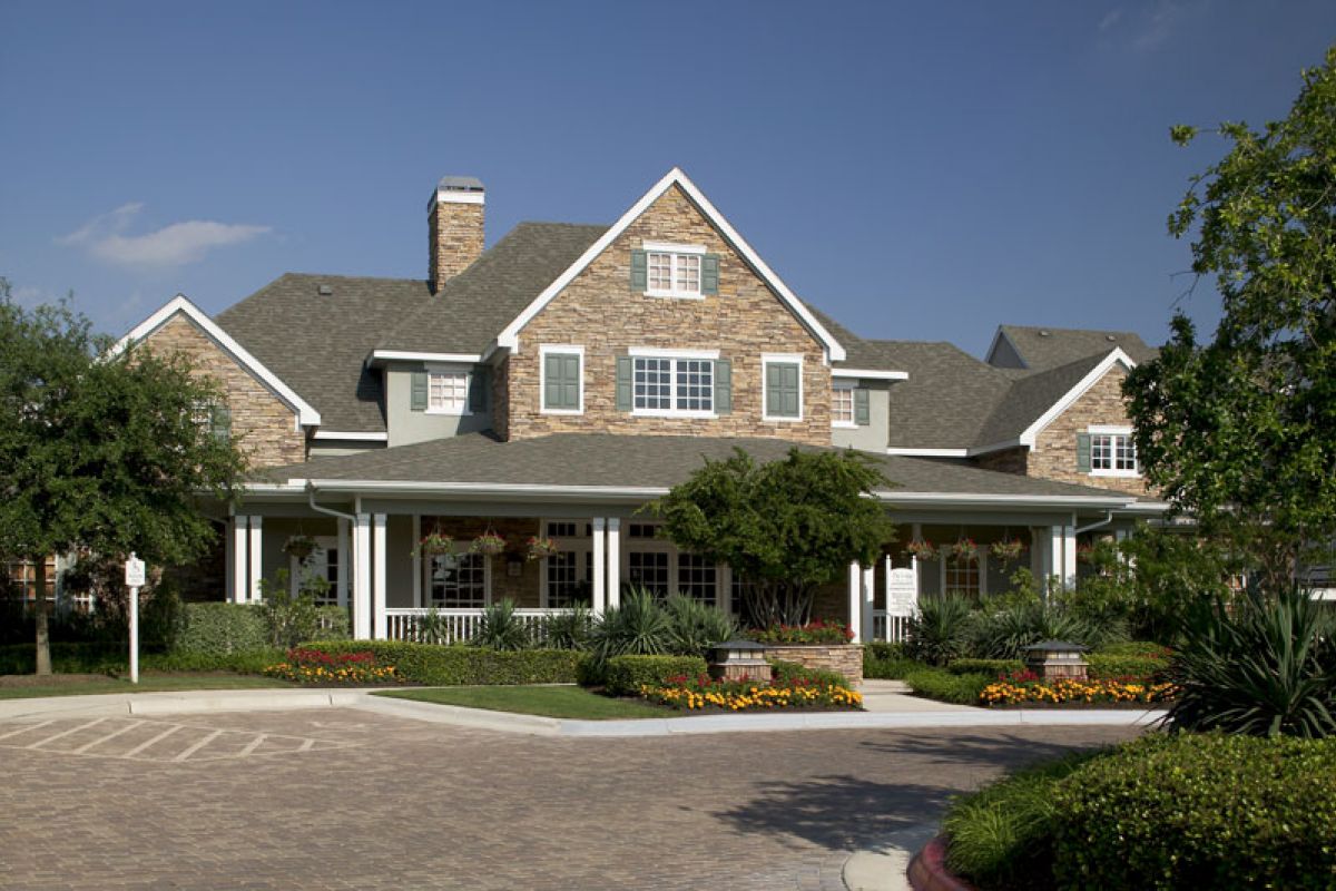 Large suburban house with stone facade, front porch, and landscaped garden under a clear blue sky.