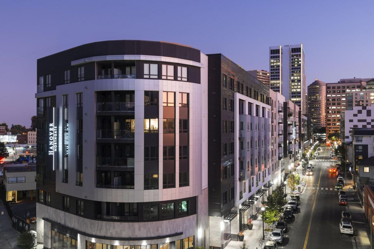 Modern multi-story building on a city street at dusk, with cars parked along the road.