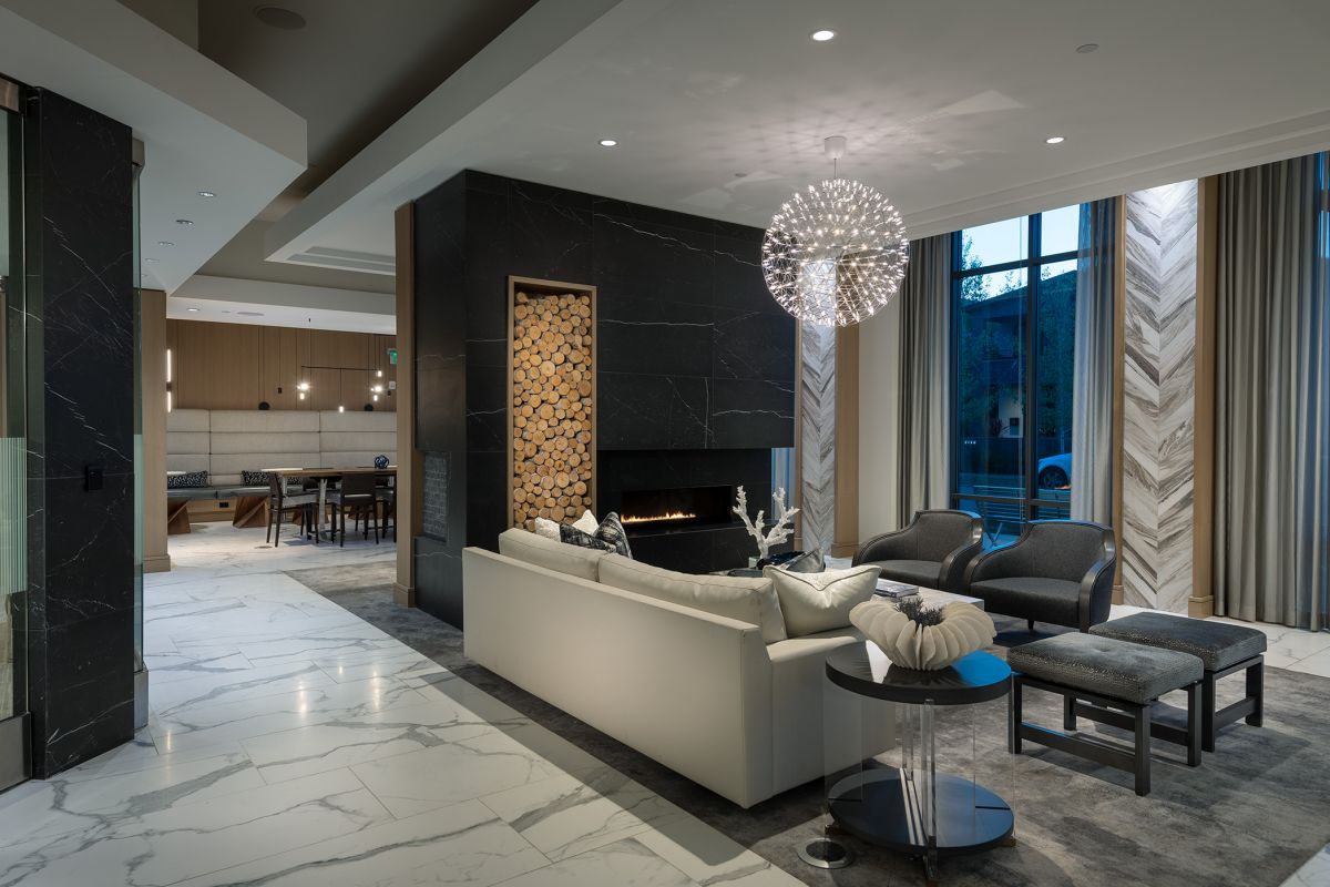 Modern living room with marble floors, a fireplace, stylish seating, and large windows with evening light.