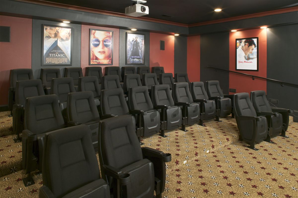 Home theater room with rows of black seats, movie posters on red walls, and a projector on the ceiling.
