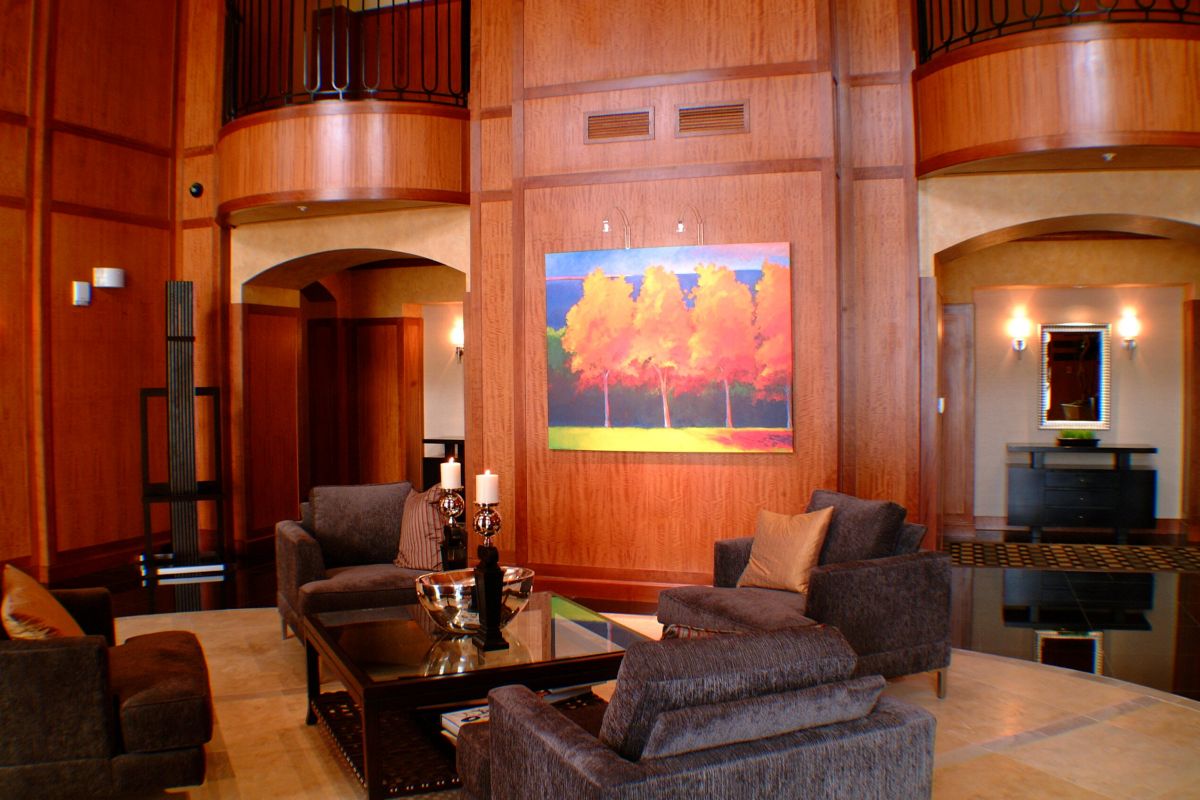 Modern living room at 1200 Post Oak with wood panel walls, gray sofas, and a colorful painting of trees above a glass coffee table.