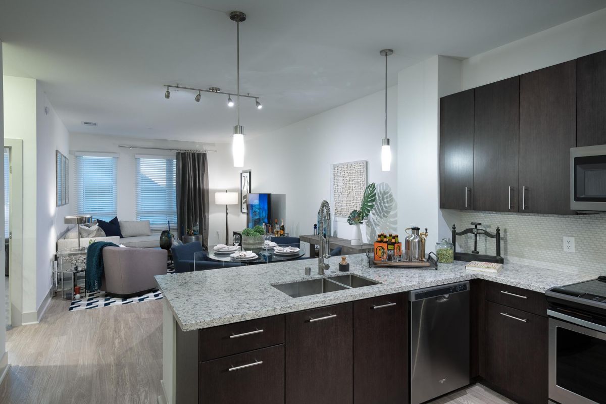 Modern kitchen with dark cabinets and granite countertops, open to a living and dining area with wood flooring.