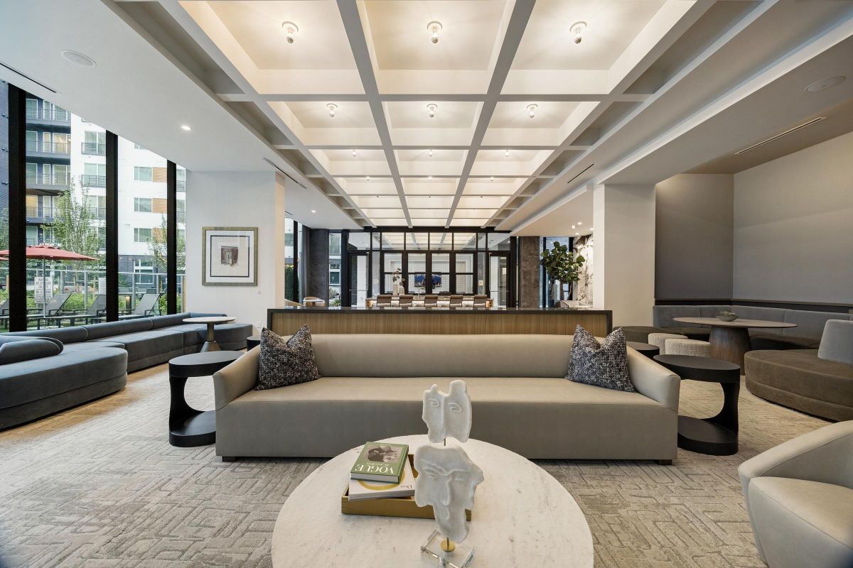 Modern lounge with beige sofas, a round table with decor, large windows, and a coffered ceiling.