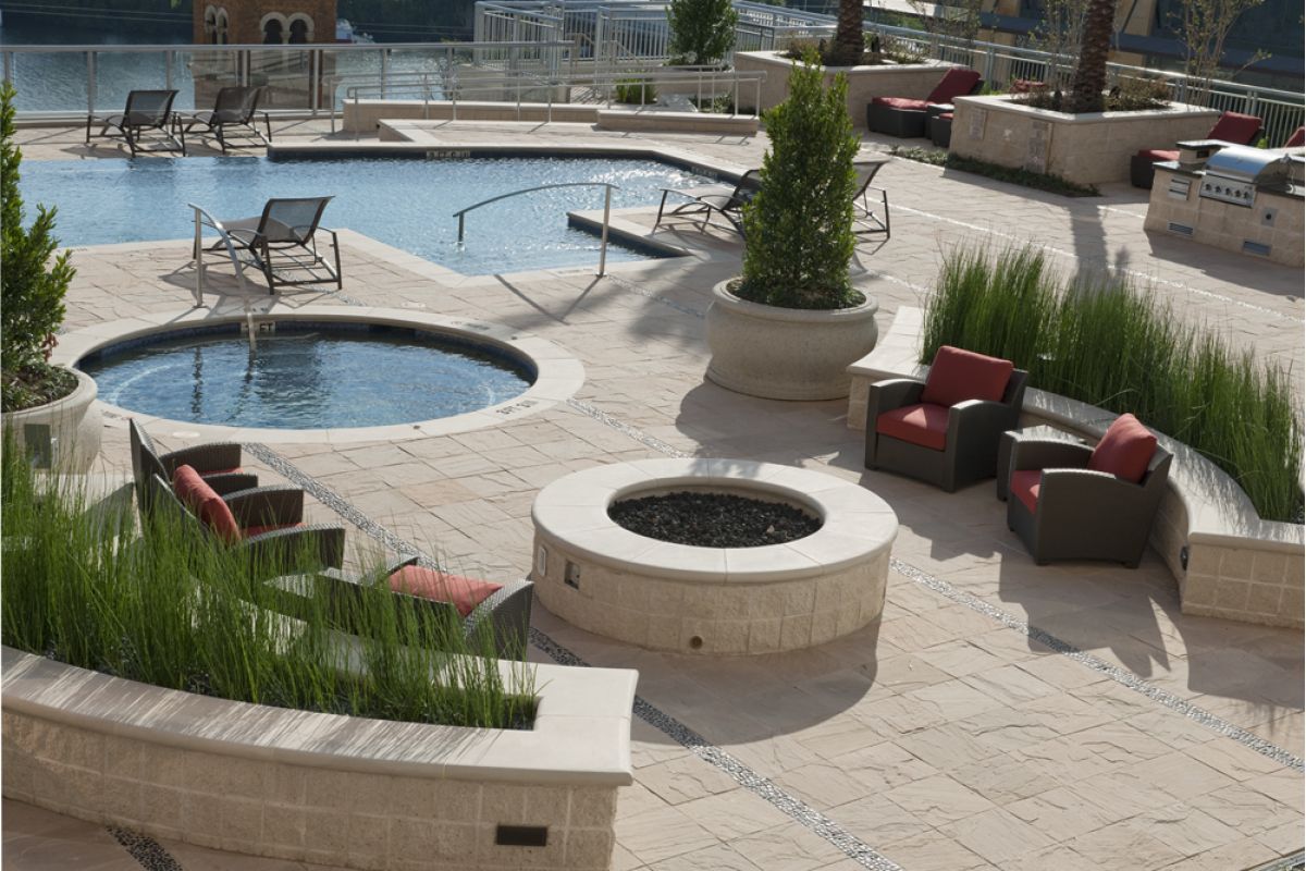 Outdoor patio at Ashton Austin with a fire pit, lounge chairs, hot tub, swimming pool, and lush green plants.