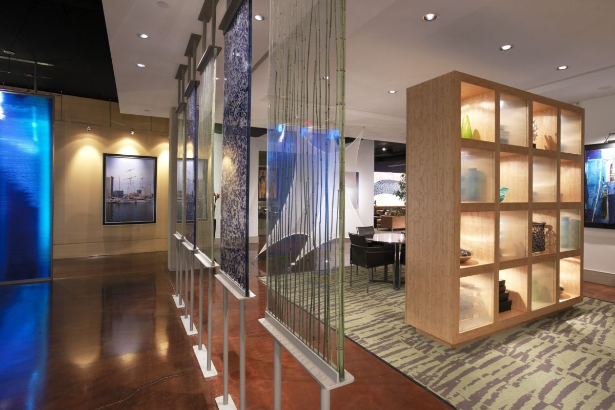 Modern office space with glass partitions, wooden display shelves, and patterned carpet flooring.