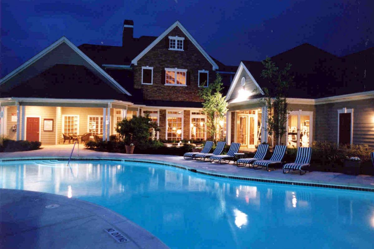 Large house with lights on at dusk, pool in foreground, lined with striped lounge chairs on the deck.