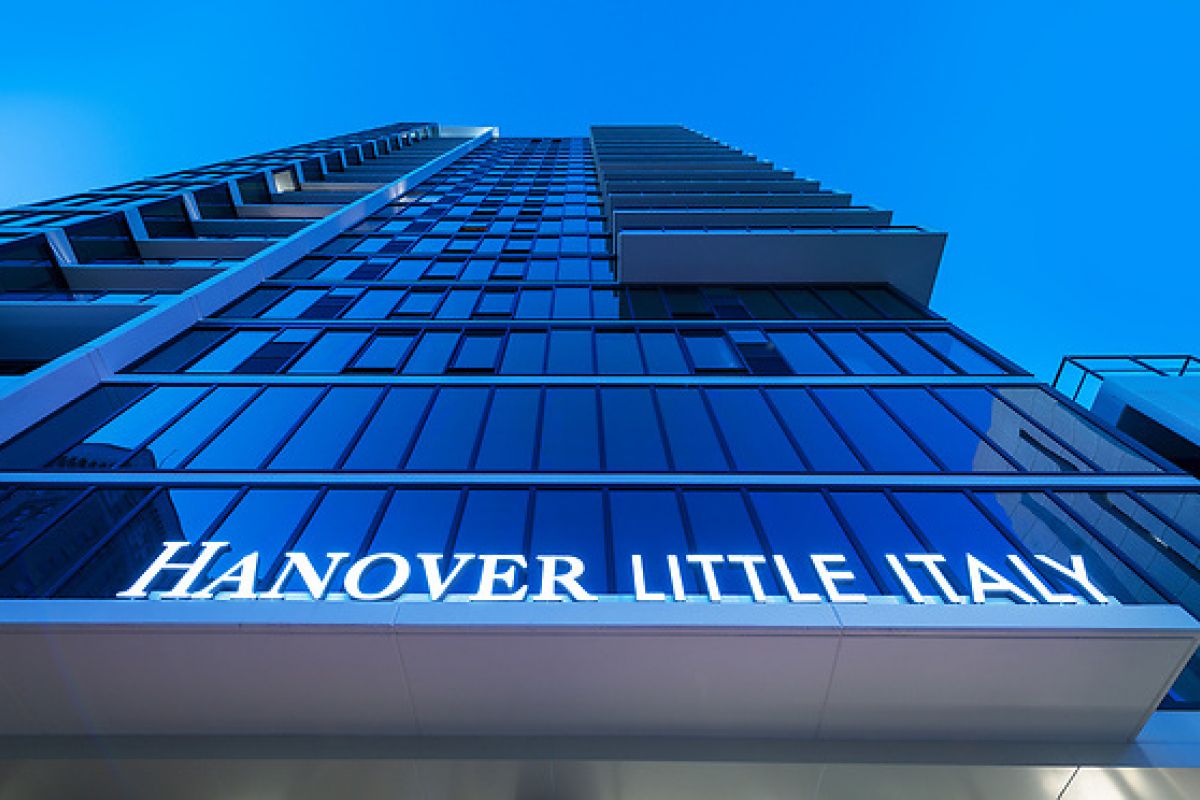 Modern high-rise building with "Hanover Little Italy" sign, photographed from a low angle against a blue sky.