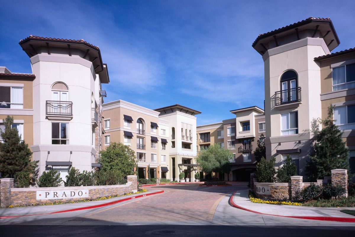 A modern apartment complex with beige buildings and a sign reading "PRADO" at the entrance.