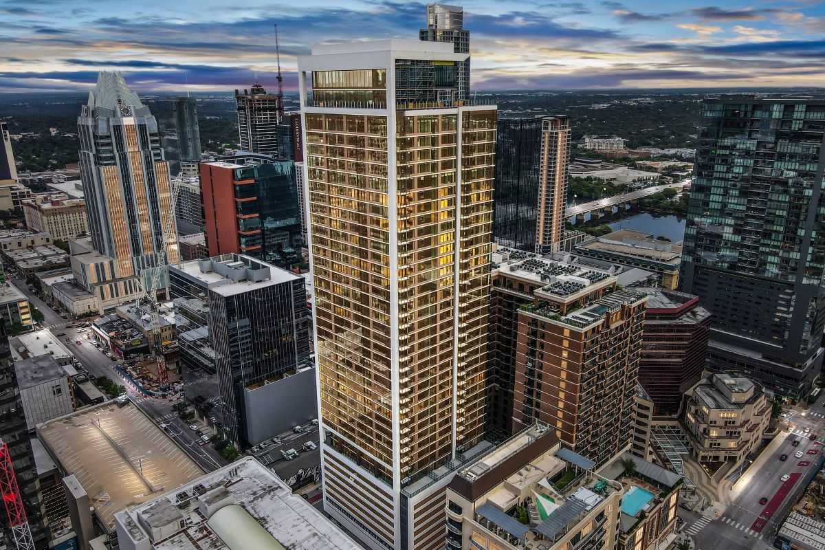 Hanover Company, Hanover Republic Square Aerial view of a city's skyscrapers at dusk, with a prominent building in the center illuminated by lights.