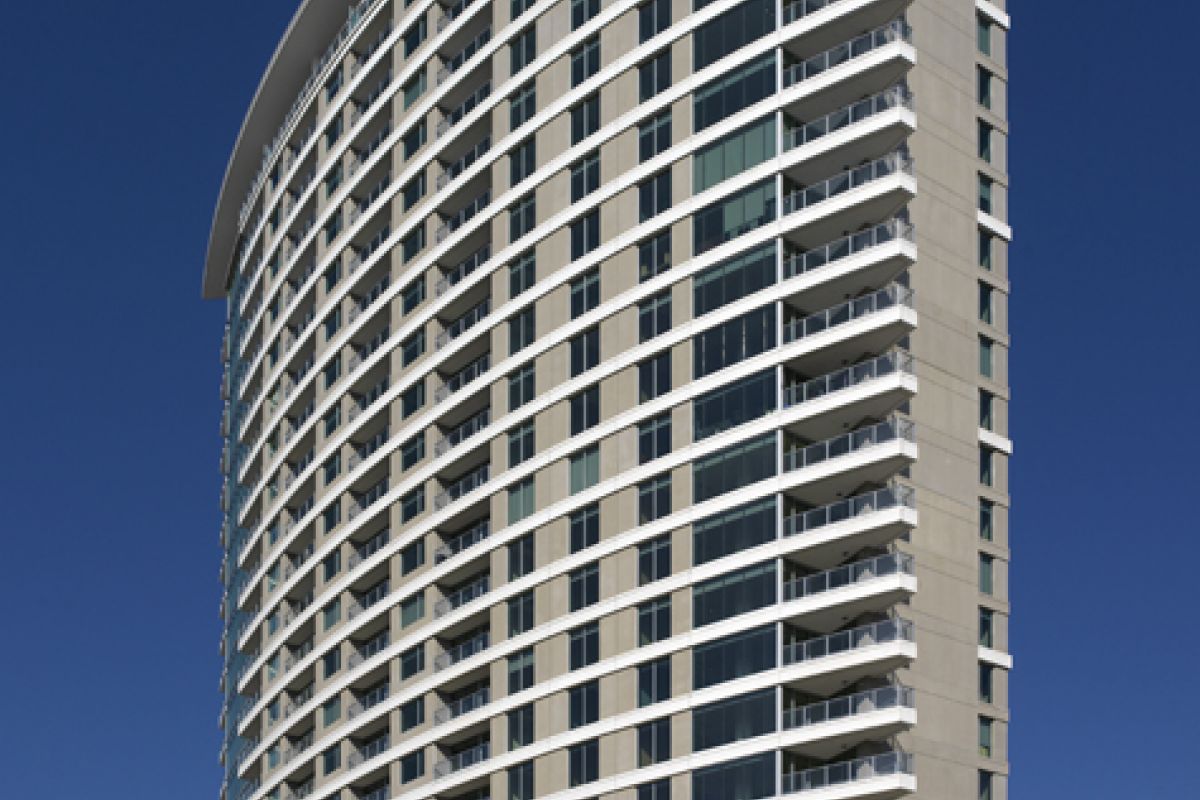 Tall, modern high-rise building with many balconies against a clear blue sky; sign reads "Cirque Luxury Living.