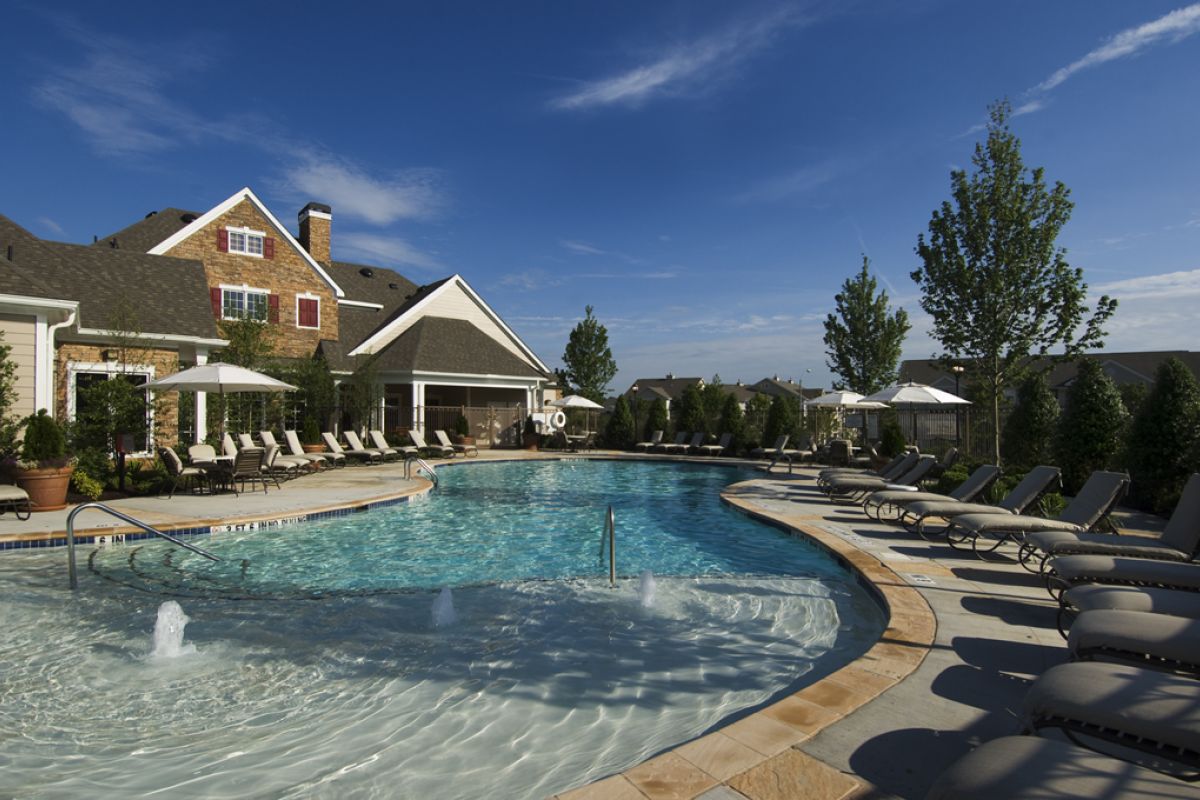 Outdoor swimming pool with lounge chairs, umbrellas, and buildings under a clear blue sky.