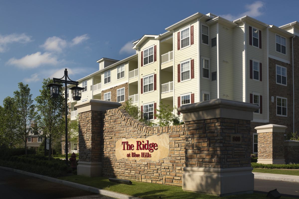 Brick sign reading "The Ridge at Blue Hills" in front of a modern, multi-story apartment building.