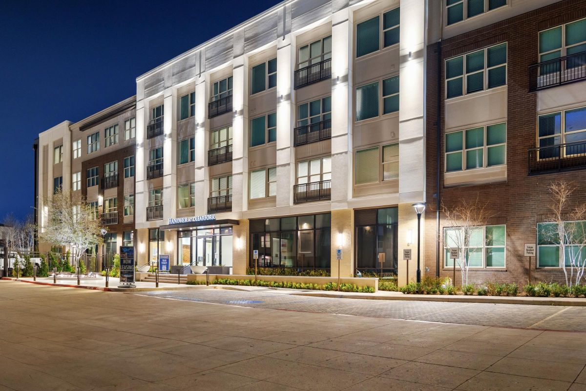 Modern apartment building exterior at night, well-lit with a clear entrance and large windows.