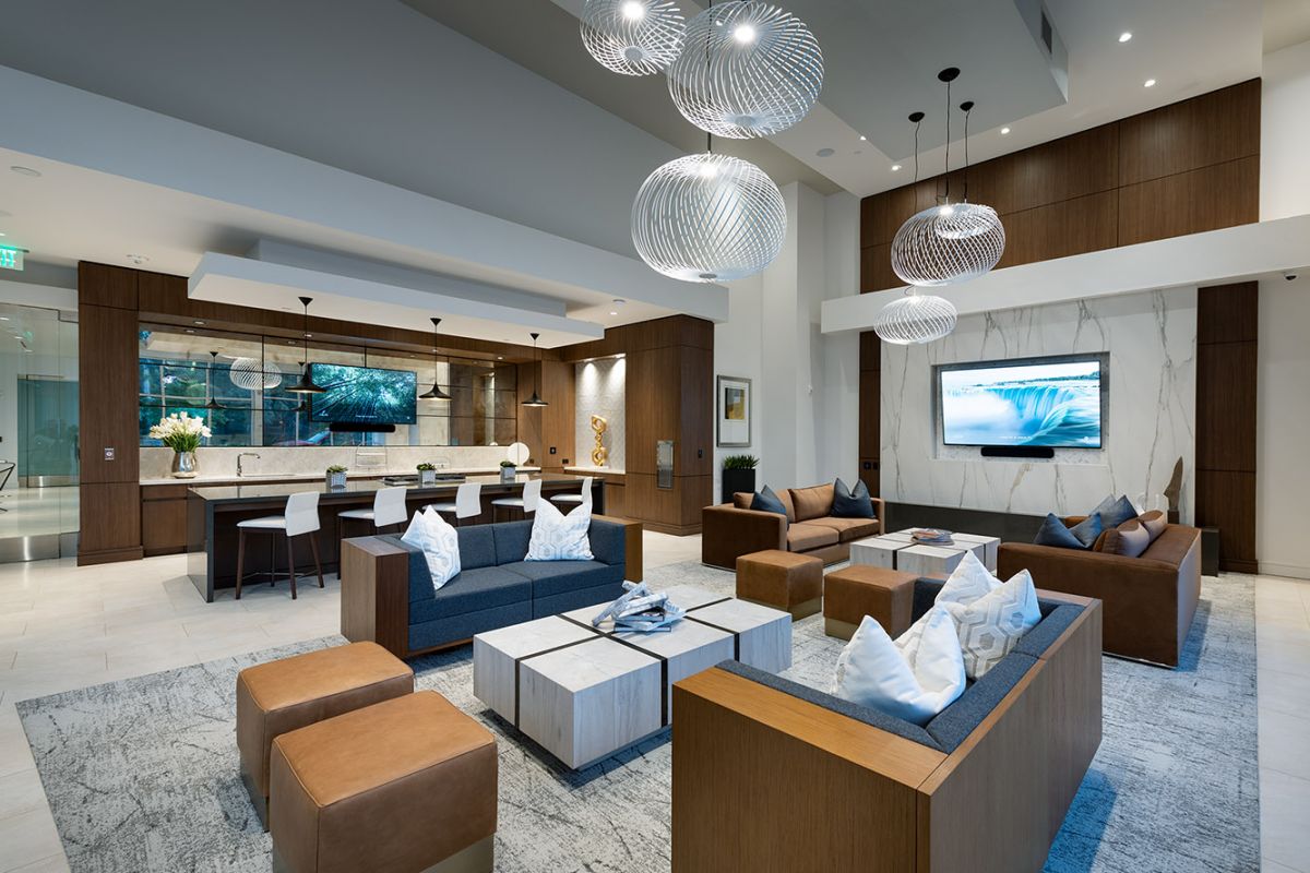 Modern lounge with sleek furniture, kitchen area, and large TV at Hanover Warner Center, decorated in neutral tones and pendant lights.