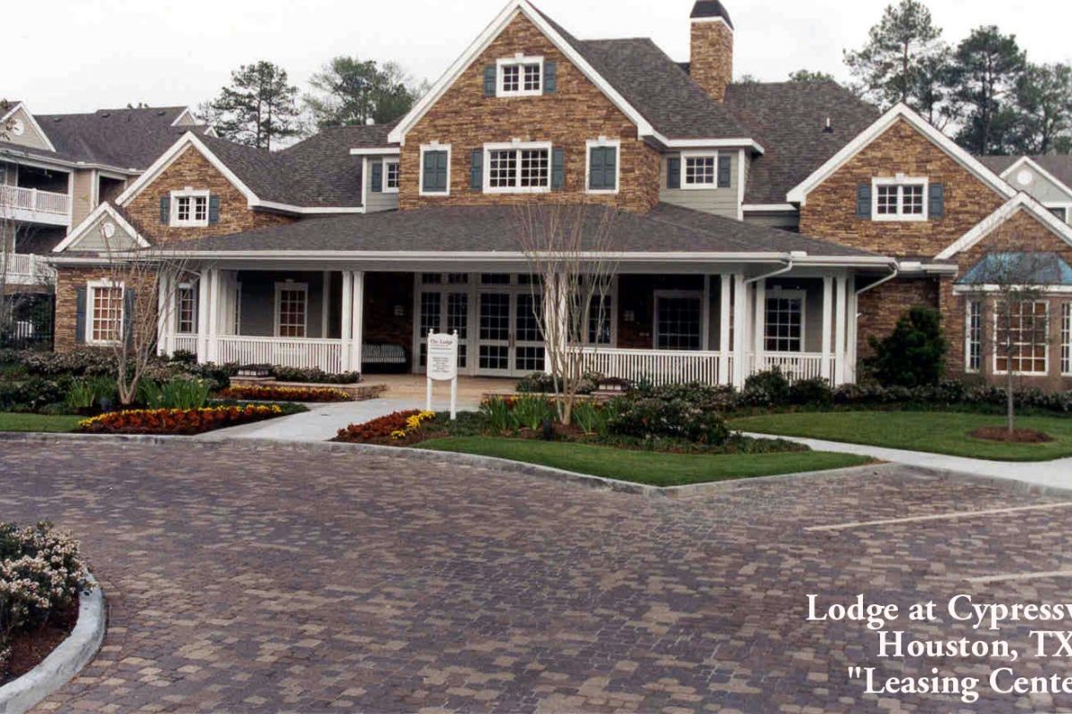 Brick building with white trim and large porch, sign in front; text reads "Lodge at Cypresswood Leasing Center" apartments in Dallas.