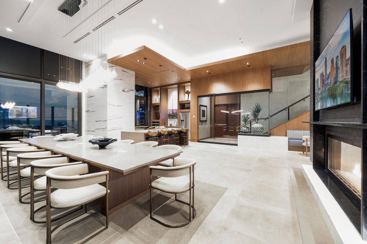 Modern dining room with a long table, white chairs, large windows, and a wall-mounted TV.