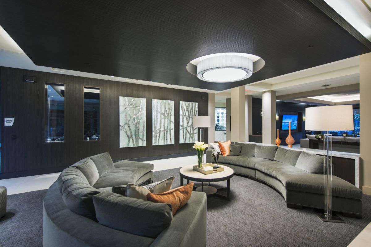 Modern lounge with curved gray sofas, round table, large ceiling light, and art on dark accent wall.