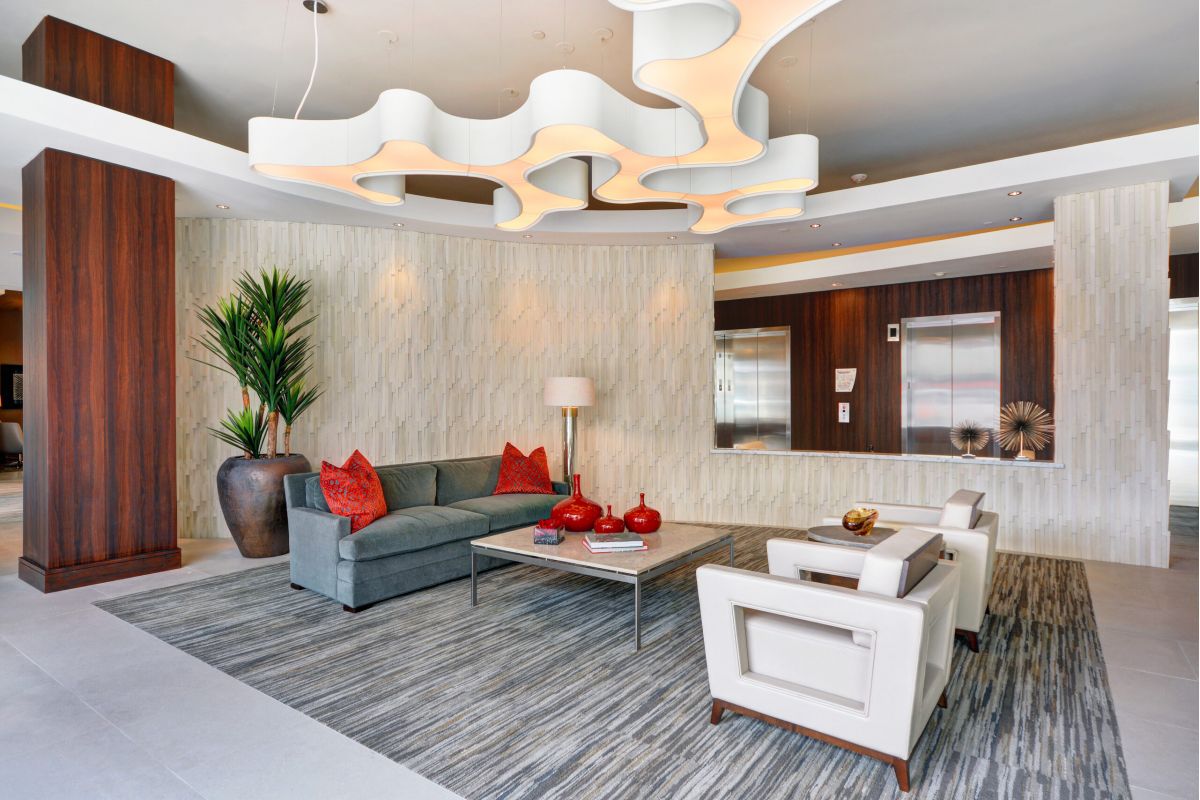 Modern lobby with gray sofa, white chairs, abstract ceiling lights, and red accent decor.