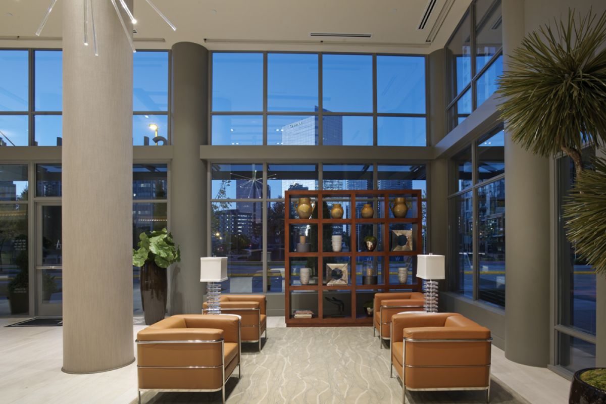 Modern lobby with tan leather chairs, large windows, city view, and decorative shelving with vases.