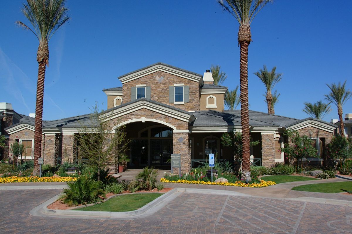 A modern building with stone walls, palm trees, and landscaped gardens under a clear blue sky.