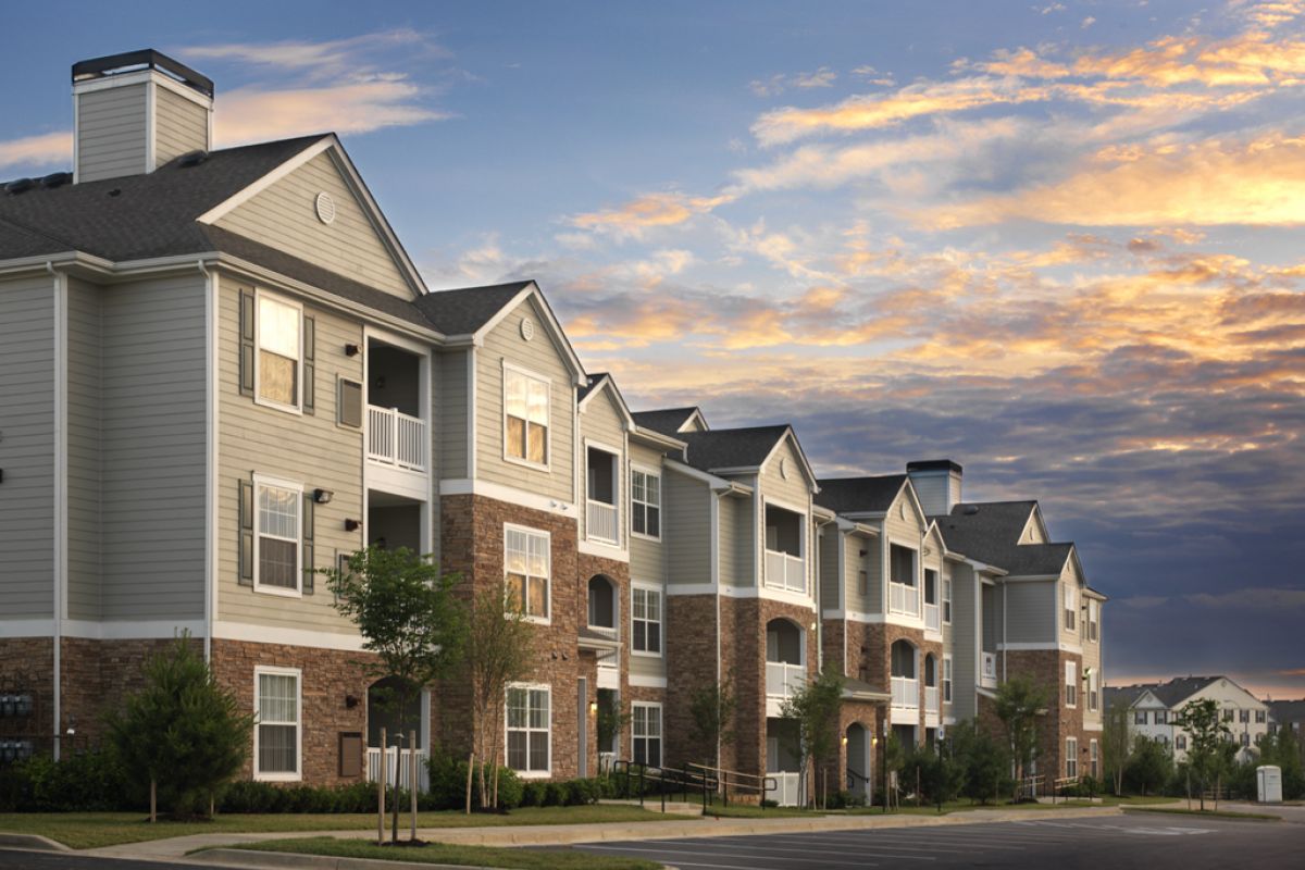 Modern apartment buildings with balconies and brick accents, under a colorful sunset sky.