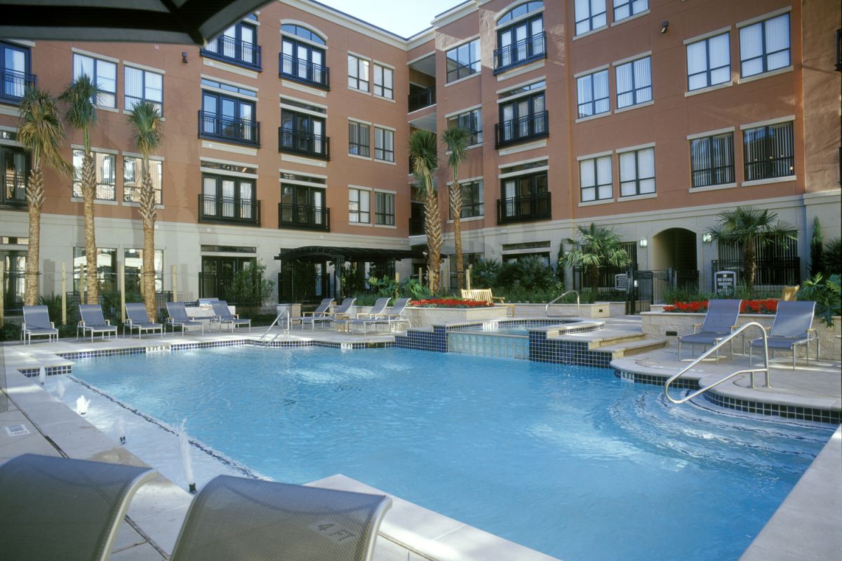 Outdoor swimming pool surrounded by lounge chairs in the courtyard of a modern apartment building.