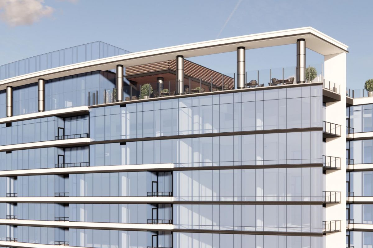 Modern glass building with balconies, featuring a rooftop terrace with plants and seating under a blue sky.