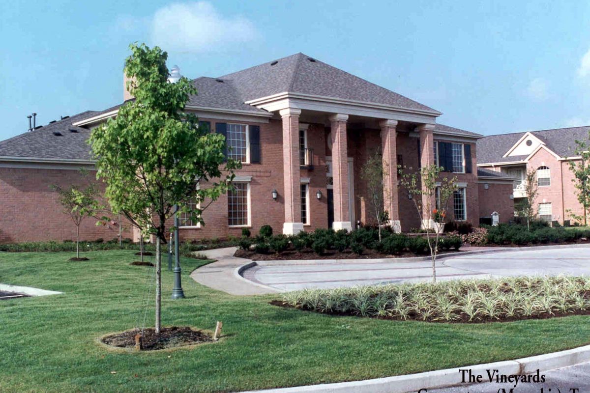 Brick building with tall columns, manicured lawn, and trees; sign reads "The Vineyards Leasing Center.