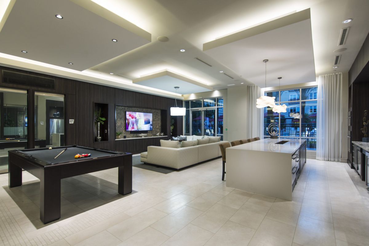 Modern open-concept living space with a pool table, white sofa, TV, and a large kitchen island.