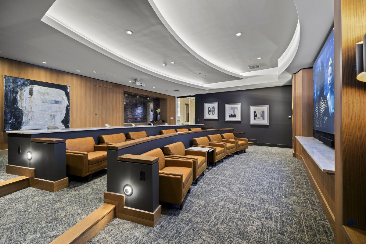 Modern home theater with curved seating, large screen, and artwork on walls. Cozy lighting with gray and brown decor.