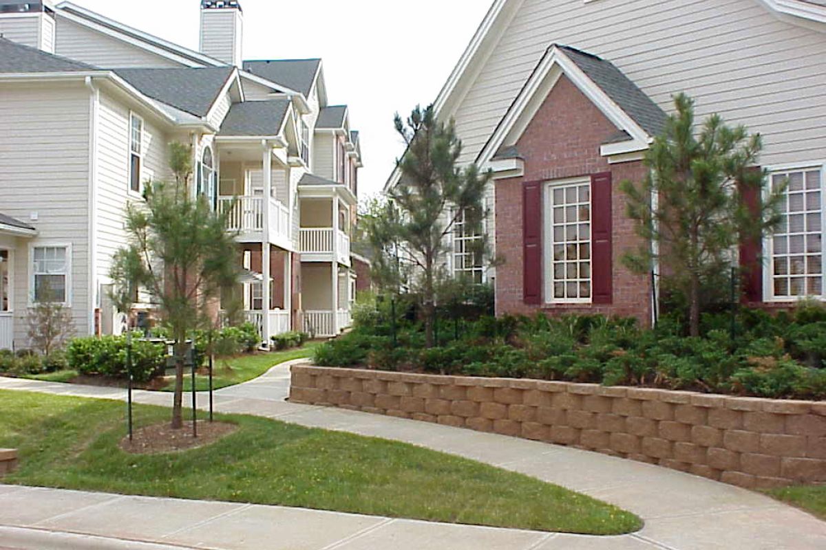 Light-colored apartment buildings with balconies, landscaped shrubs, and a curved sidewalk in front.