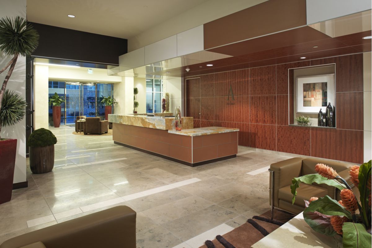 Modern office lobby with a marble reception desk, brown seating, plants, and large windows letting in natural light.